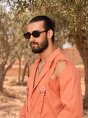 GANGO — homme en lunettes de soleil, léger sourire bouche fermée, ambiance automne naturelle.